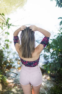 Rear view of teenage girl with hand in hair standing against lake