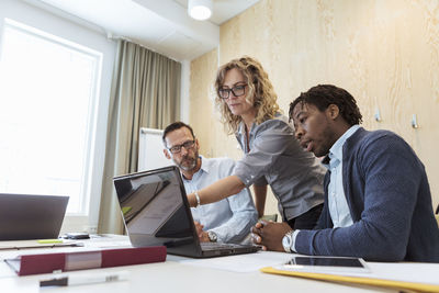 Mature businesswoman pointing at laptop while working with colleagues in board room