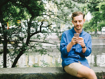 Young man using mobile phone by canal