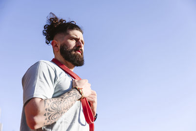 Bearded man with resistance band under blue sky