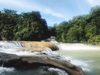 Scenic view of waterfall in forest against sky