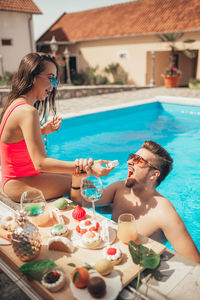 Young beautiful couple eating cookies by the pool. funny moments.