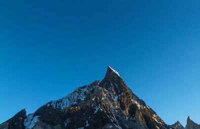 Low angle view of snowcapped mountains against clear blue sky