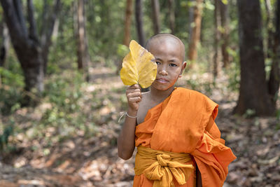 Portrait of smiling monk holding leaf while standing in forest