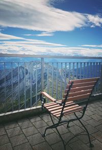Empty chairs on railing by sea against sky