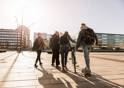 Teenage boy skateboarding while girl walking with bicycle and friends in city