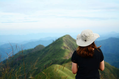 Rear view of woman wearing hat looking at mountains against sky