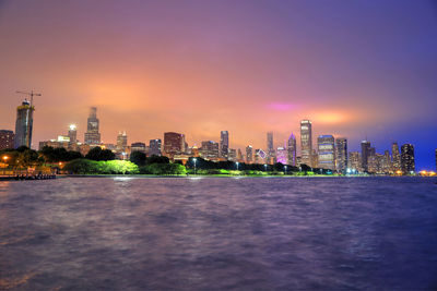 Illuminated modern buildings in city against sky during sunset