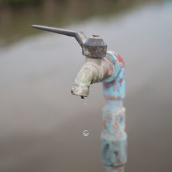 Close-up of water drop falling from metallic faucet