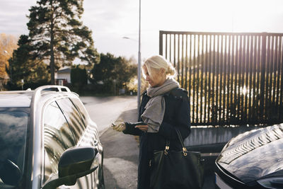 Mature woman standing by car against sky