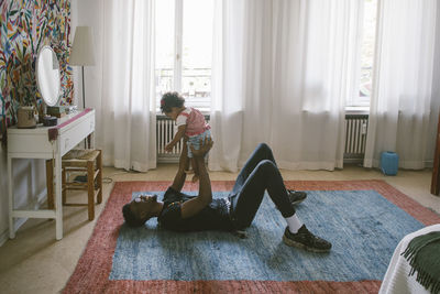 Playful father lifting daughter while lying on carpet at home