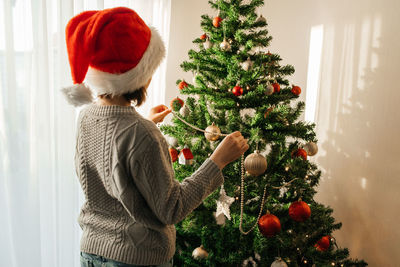 New year's and christmas. a teenage girl in a santa claus hat decorates the christmas tree 