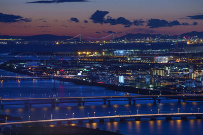 Illuminated bridge over river by buildings in city at night