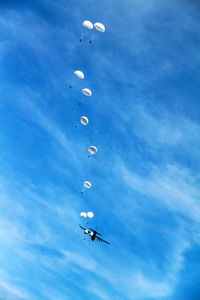 Low angle view of airplane and parachutes flying against blue sky