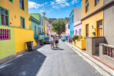 Rear view of people walking on road amidst buildings in city