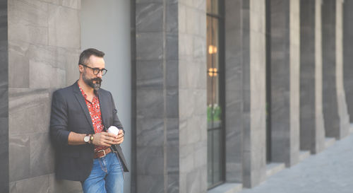 Man leaning on wall while holding coffee cup