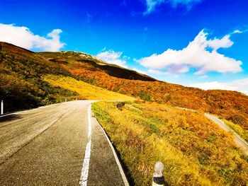 Road leading towards mountain with autumn leaves against sky