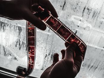 Cropped hands of person holding negative film by wet window