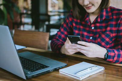 Midsection of woman using mobile phone while sitting on table