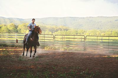 Full length of man riding horse in pen against clear sky