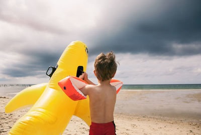 Boy playing on beach against cloudy sky