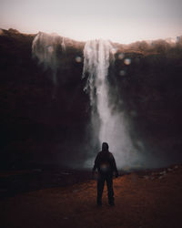 Rear view of man looking at waterfall against sky