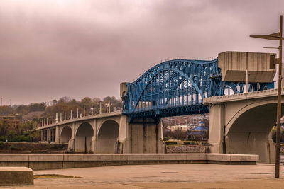 Arch bridge over river against cloudy sky
