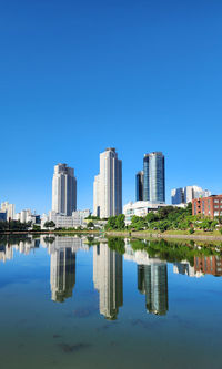 Reflection of buildings in water against clear blue sky
