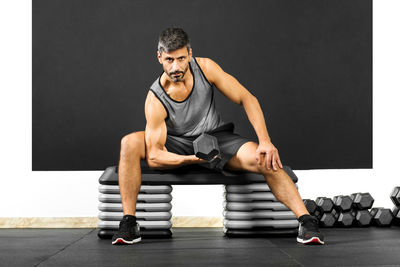 Portrait of man exercising with dumbbell against wall