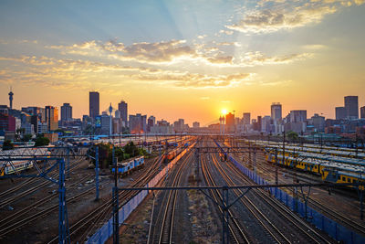 Railroad tracks in city against sky during sunset