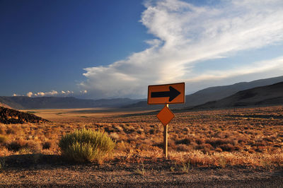Road sign on landscape against sky