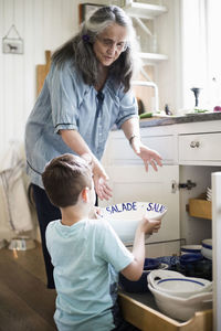 Boy giving utensil to grandmother in kitchen at home