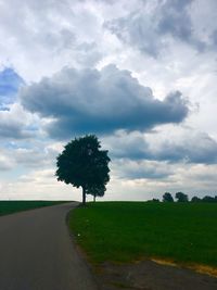 Road by trees on field against sky