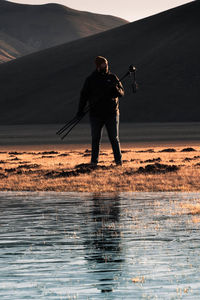 Full length of man standing on sea against sky during sunset