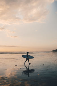 Silhouette man with surfboard walking at beach during sunset