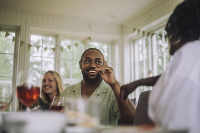 Happy mature man gesturing while talking to female friend during party at home