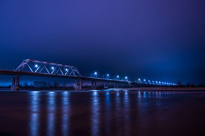 Low angle view of illuminated bridge over frozen river at night