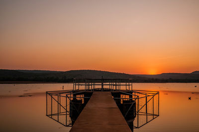 Pier over sea against orange sky