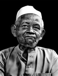 Close-up portrait of man wearing hat against black background