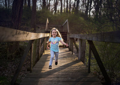 Gorgeous young girl long curls smiling and running down bridge