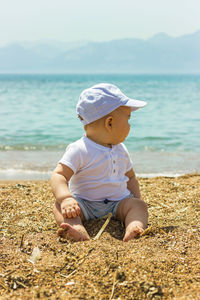 Portrait of boy sitting at beach against sky