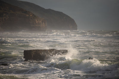 Waves splashing on rocks against sky