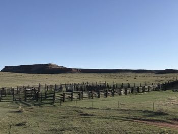 Wooden fence on field against clear blue sky