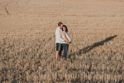 Smiling man touching pregnant girlfriend belly while standing on field