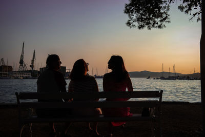 Rear view of family sitting by sea on bench during sunset