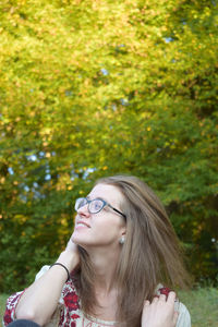 Smiling young woman looking away while sitting against trees in park