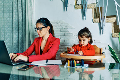 Young executive woman working from home while taking care of her young daughter