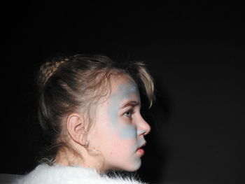 Girl with messy face looking away against black background