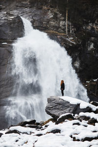 Side view of traveling woman standing on rock and observing amazing view of powerful waterfall in highlands in winter