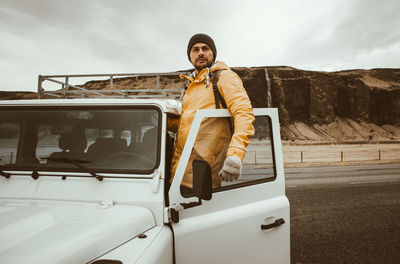 Portrait of man standing by car against sky